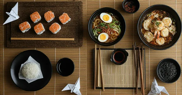 Authentic Japanese cuisine with assorted fresh sushi, steaming ramen with chashu, crispy tempura, and takoyaki octopus balls displayed with ceramic sake set, origami crane, and kokeshi doll on bamboo surface