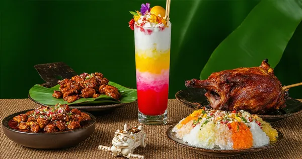 Authentic Filipino cuisine with pork adobo, sizzling sisig, colorful halo-halo, and crispy lechon displayed with capiz shell decoration, buri fan, and wooden kalesa model on rattan surface