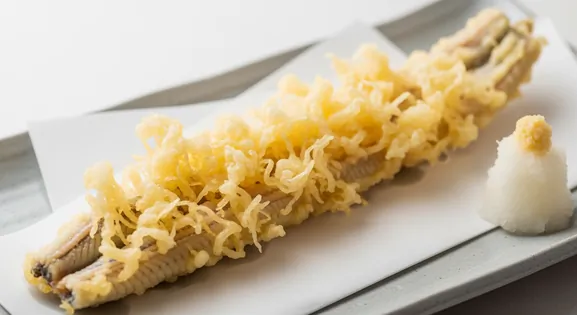 Close-up of a delicate, golden-brown Anago Tempura (conger eel) fillet from Japan, showcasing its light, crispy batter...
