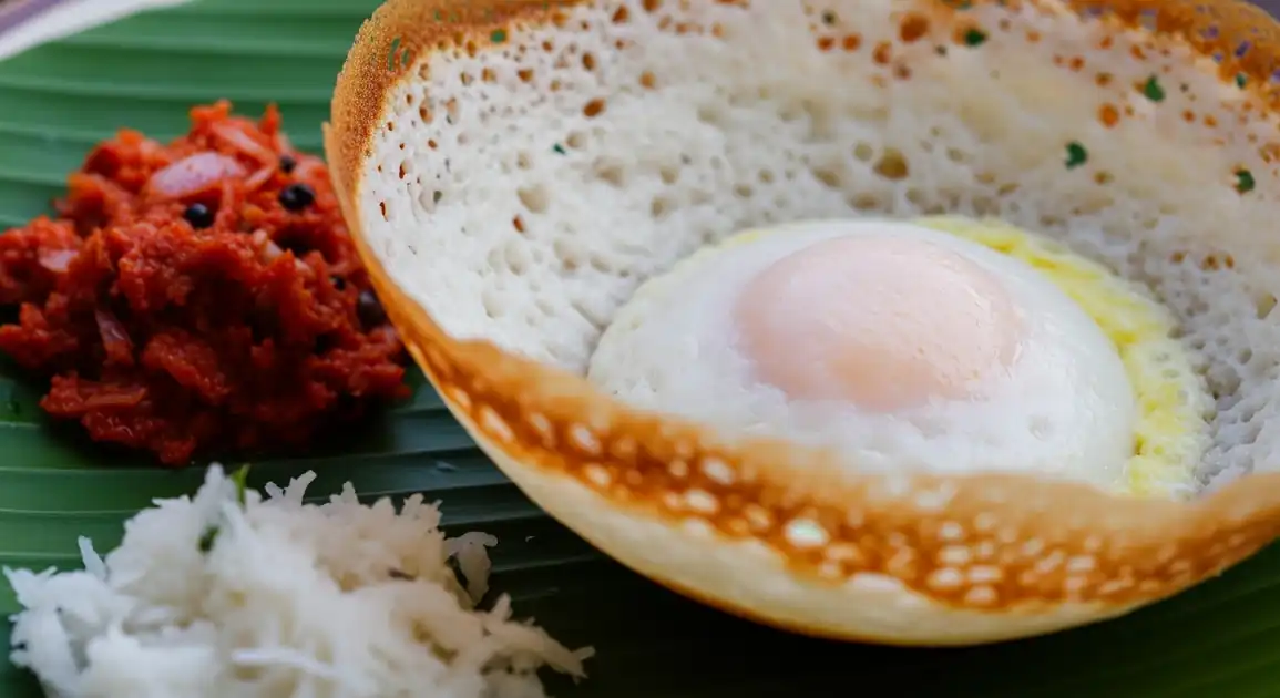 Authentic Sri Lankan Appam (Hopper), bowl-shaped with crispy lace edges and soft center, possibly holding an egg, served...